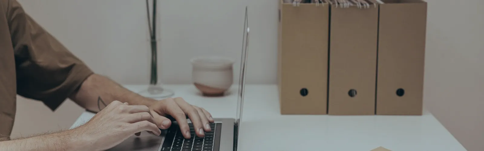 Hands on a laptop, archive boxes on a desk