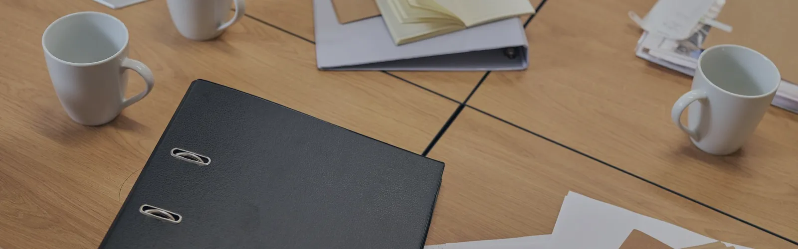 Binder, mugs and loose papers on a meeting table