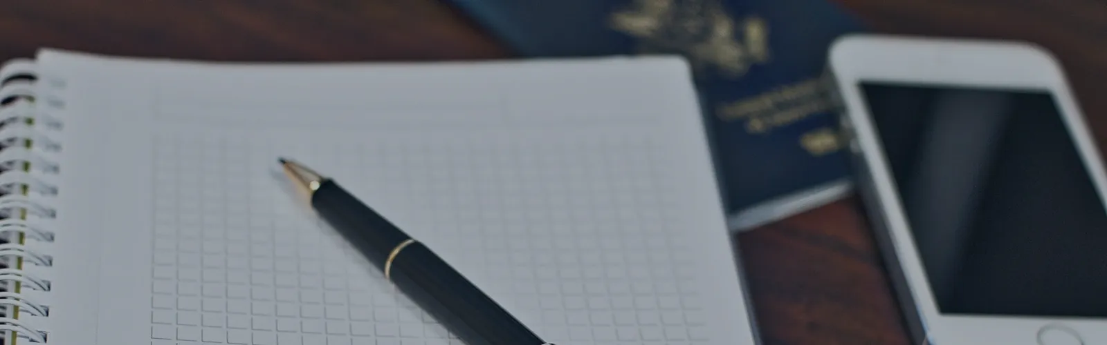 Stylo posé sur un carnet quadrillé vierge, passeport fermé en arrière-plan